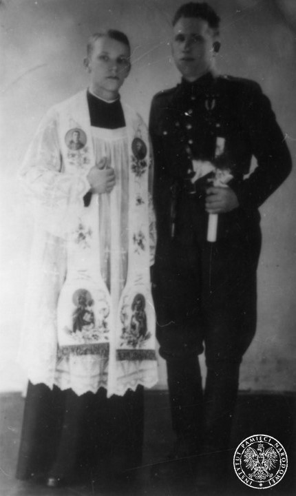 Jezuita ojciec Władysław Gurgacz z nieznanym żołnierzem armii komunistycznej, w dniu jego chrztu (13 czerwca 1946 roku). Mężczyzna nawrócił się pod wpływem nauk głoszonych w szpitalu, w którym funkcję kapelana pełnił ojciec Gurgacz. Jezuita ubrany jest w sutannę, komżę i stułę z wizerunkami Maryi. Żołnierz ubrany jest w mundur. W lewej ręce trzyma świecę od chrztu.