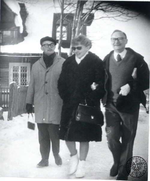 Stefan Kisielewski z żoną Lidią podczas wypoczynku w Zakopanem, koniec listopada 1966 roku. Na zdjęciu, zrobionym przez tajne służby PRL inwigilujące Kisielewskiego (a właściwie jego i jego rodzinę), znalazł się też mężczyzna z hotelu, w którym Kisielewscy wtedy przebywali. Zdjęcie wykonane w scenerii już zimowej. Ulicą idą trzy osoby. Szeroko uśmiechający się Stefan Kisielewski trzyma, także śmiejącą się, żonę pod rękę (pod drugą ręką przytrzymuje książkę). Drugi mężczyzna, w okularach, w szczelnie zapiętym ciepłym płaszczu, w berecie, z szalikiem pod szyją i w rękawiczkach, idzie nieco za nimi. Lidia Kisielewska, niosąca damską torebkę, także jest ubrana ciepło, w zapięty gruby, wełniany płaszcz, biały szal pod szyją i białe trzewiki. Stefan Kisielewski, noszący grube okulary, ma natomiast rozpiętą lekką kurtkę, odkrytą głowę, ubrany jest ponadto w białą koszulę z krawatem i sweter. W tle zabudowa wiejska (w stylu góralskim).