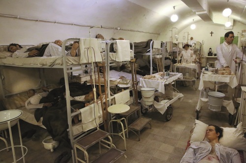 Rekonstrukcja sali dla chorych w Muzeum Szpitala w Skale. Manekiny pacjentów ułożone na metalowych, piętrowych łóżkach.
