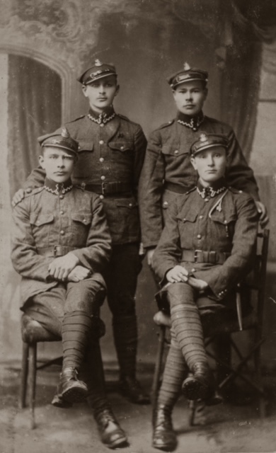 Mikołaj Nycz z kolegami z 1. kompanii 10. Batalionu Sanitarnego w Przemyślu koniec 1922 roku. Na pozowanym zdjęciu widać czterech mężczyzn w mundurach; dwóch z nich siedzi na krzesłach, dwóch innych - stoi za nimi.