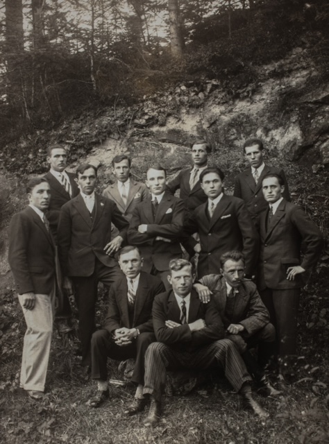 Członkowie Związku Strzeleckiego w latach trzydziestych XX wieku. W środku stoi Mikołaj Nycz. Zdjęcie zrobione w leśnym wąwozie. Na zdjęciu jest dwunastu mężczyzn, z których większość stoi, a trzech siedzi na ziemi. Mężczyźni ubrani są w koszule, krawaty i marynarki.