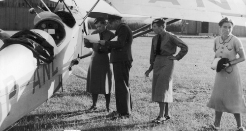 Wanda Modlibowska (1. z lewej) oraz Ewa Korczyńska (4. z lewej) z Aeroklubu Poznańskiego w otoczeniu nierozpoznanych osób, przed startem w Krajowych zawodach lotniczych na Lotnisku Mokotowskim w Warszawie, sierpień 1938 r. Fot. ze zbiorów NAC