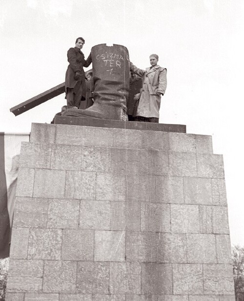 Po obaleniu potężnego pomnika Stalina na cokole zostały tylko buty. Na bardzo wysokim cokole, przy kamiennym bucie, stoi kilka osób, z których dobrze widoczni są dwaj mężczyźni ubrani w płaszcze.