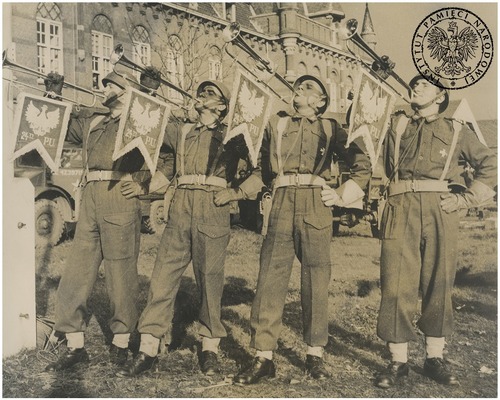 Trębacze z 24. Pułku Ułanów 1. Dywizji Pancernej grają na trąbkach sygnalizacyjnych w zajętej Bredzie. Na proporcach orzeł i nazwa „24ty P.U.”. Autor: nieznany. Breda, październik-listopad 1944 r. (fot. z zasobu IPN)