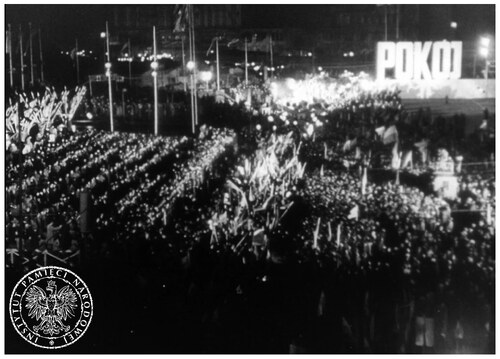 Wielka, licząca 150 tysięcy osób, manifestacja na placu Zwycięstwa w Warszawie w obronie pokoju na świecie, którą komuniści zorganizowali w trakcie II Światowego Kongresu Obrońców Pokoju (Warszawa, 16-21 listopada 1950 roku). Na zdjęciu, zrobionym już po zmierzchu, widać bardzo wielu ludzi idących w pochodzie złożonym z przodu z ludzi jakby swobodniej maszerujących, za którymi zmierza kolumna ludzi ustawionych w równych, żołnierskich rzędach. Widoczne liczne sztandary. W głębi widać, postawione na jakimś budynku, duże litery składające się na słowo: „POKÓJ”. Kadr z propagandowego filmu pod tytułem „Droga walki” zrealizowanego w Biurze „B” Wydziału XII komunistycznego Ministerstwa Spraw Wewnętrznych.