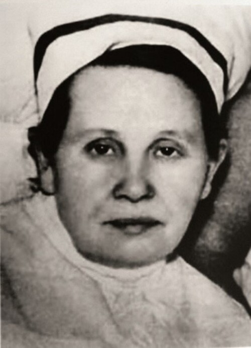 Stanisława Leszczyńska. Na zdjęciu jest jeszcze młoda kobieta o dobrym, matczynym, ale smutnym obliczu. Kobieta ubrana jest w biały kitel i ma na głowie czepek pielęgniarski zakrywający ciemne włosy.