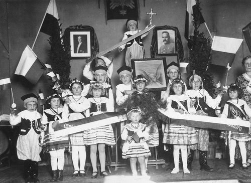 Grupa polskich dzieci w Szczecinie, 1930 r. Fot. z zasobu NAC. Dzieci w strojach ludowych. Widoczne flagi polskie, na ścianie wiszą portrety Józefa Piłsudskiego i Ignacego Mościckiego.