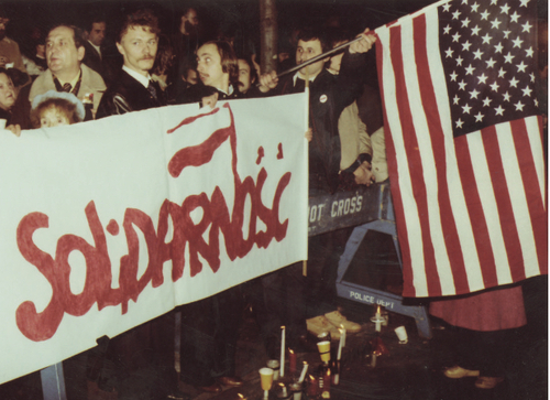 Zdjęcie z demonstracji ulicznej. Widoczny transparent z napisem: Solidarność oraz flaga Stanów Zjednoczonych