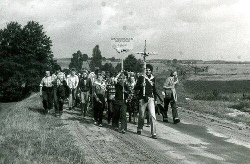 Pierwsza zorganizowana pielgrzymka piesza z Lęborka do Sianowa, 13 września 1980 roku. Ze zbiorów księdza Mariana Miotka. Na zdjęciu jest widoczna grupa pielgrzymkowa - kobiety i mężczyźni - idąca polną drogą. Wśród pielgrzymów przeważają młodzi i bardzo młodzi ludzie. Na czele grupy jedna osoba, młody mężczyzna, niesie prosty, brzozowy krzyż, zaś druga, młody chłopak, tablicę, na której jest napisane: „Do Królowej Kaszub pielgrzymuje Lębork” .