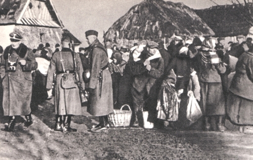 Polacy wysiedlani z Zajmojszczyzny, grudzień 1942 r. Wieśniacy gromadzący się z tobołkami pod nadzorem uzbrojonych niemieckich funkcjonariuszy. W tle wiejskie chaty.