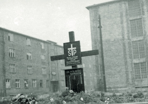 Prowizoryczny krzyż na tle budynków więziennych