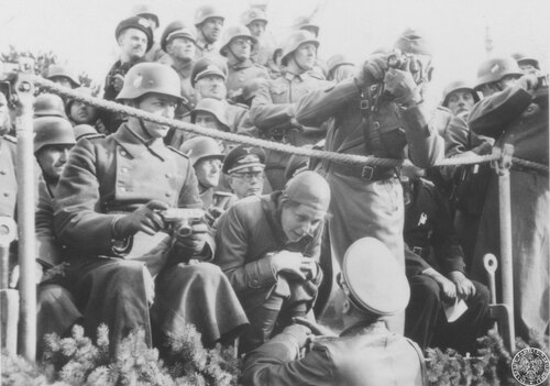 Leni Riefenstahl - wśród licznych oficerów niemieckich - kucając rozmawia z oficerem stojącym przed trybuną w Alejach Ujazdowskich