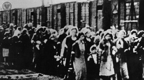 Grupa kobiet i dzieci idących przez Umschlagplatz do wagonów towarowych