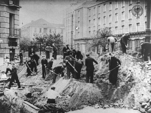 Mężczyźni kopią rów przeciwlotniczy na rogu ulic Targowej i Wileńskiej w Warszawie we wrześniu 1939 r. Po lewej narożnik kamienicy przy ul Targowej 75. W głębi, po prawej, za ulicą Wileńską, budynek Dyrekcji Kolei Państwowych