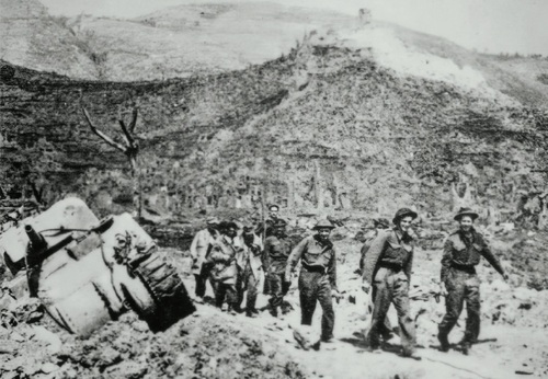 Polscy żołnierze niosą i prowadzą rannych. Na drugim planie klasztor na Monte Cassino. Po lewej zniszczony czołg M4 Sherman. Fotografia zamieszczona w pierwszym wydaniu książki Melchiora Wańkowicza <i>Bitwa o Monte Cassino</i>. Pod zdjęciem podpis: Znosili z gór swych rannych kolegów i drogo płacili krwią. Fot. AIPN