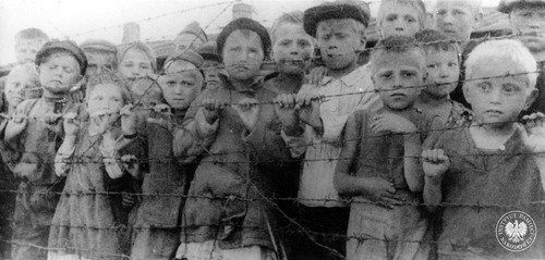 Dzieci za drutami niemieckiego obozu (wg części źródeł podczas czasowego pobytu w KL Auschwitz-Birkenau). Prawdopodobnie są to dzieci pochodzące z terenów Związku Sowieckiego lub Polski umieszczone w obozie przed wywiezieniem do Niemiec do pracy lub w celach germanizacji (w ramach akcji „Heuaktion”) – lipiec 1944 r. (fot. z zasobu AIPN)