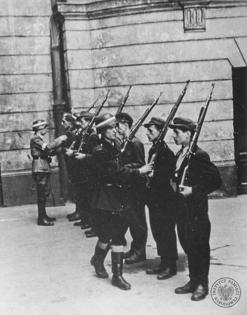 Oddział „Koszta”, nauka obchodzenia się z bronią. Na pierwszym planie przed szeregiem – Jerzy Tyczyński „Jur”. Od prawej w szyku stoją: strzelec Janusz Chyliński „Góral”, kapral podchorąży Ryszard Ryng „Dick” oraz starszy strzelec podchorąży Tadeusz Szmigiera „Wład” (fot. z zasobu AIPN, autor: Eugeniusz Lokajski)