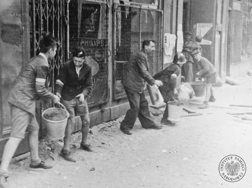 Gaszenie pożaru, chłopcy podają wodę. Widoczne opaski powstańcze (fot. z zasobu IPN)