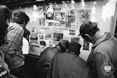 Robotnicy – pracownicy stoczni – przy tablicy ogłoszeń, na której widać liczne artykuły z prasy zagranicznej (szwedzkiej, niemieckiej, francuskiej) poświęcone strajkom w Polsce. Gdańsk, sierpień 1980 r. Fot. Stanisław Składanowski (fot. z zasobu IPN)