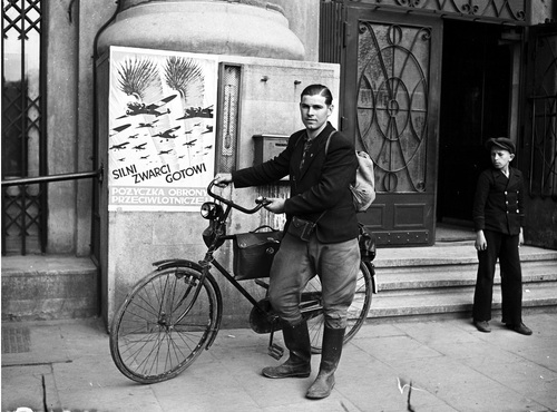 Polak z Danii Józef Andrzejczak podczas zwiedzania Polski na rowerze. Widoczny plakat z napisem: "Silni, zwarci, gotowi. Pożyczka Obrony Przeciwlotniczej", kwiecień 1939 r. (zbiory Narodowego Archiwum Cyfrowego)