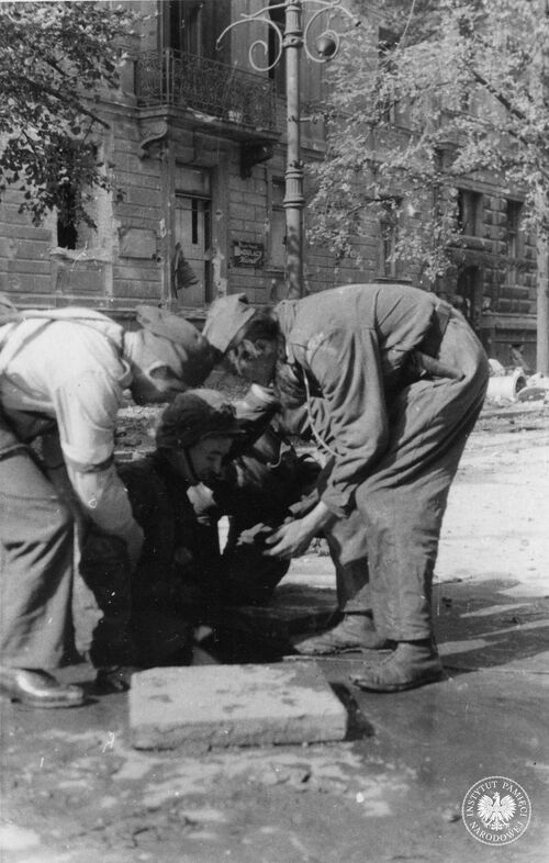 Jeden z powstańców wychodzący z kanału przy rogu ul. Wilczej i Al. Ujazdowskich, pomagają mu wachm. „Zemsta” i kpr. pchor. „Prus”. Warszawa, 27 IX 1944 r. Autor: Sylwester Braun „Kris” (fot. z zasobu IPN)