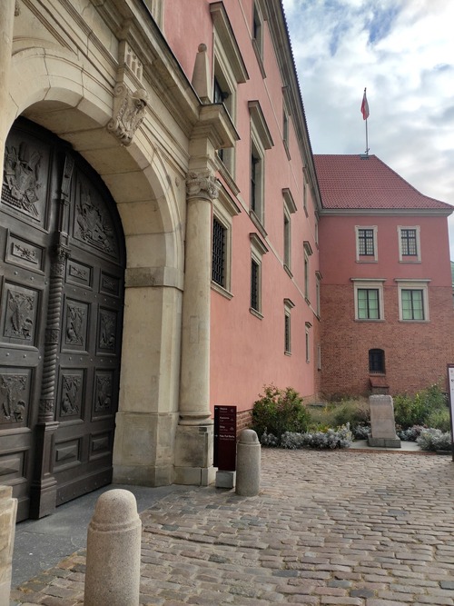 Fragment murów odbudowanego Zamku Królewskiego od południa, od strony Trasy W-Z. Na pierwszym planie widoczna Brama Grodzka, nieopodal której zginął Kazimierz Brokl, w głębi upamiętniający go obelisk. Warszawa, 2023 r. (fot. Irena Siwińska)