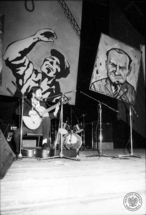 Przemysław Gintrowski podczas I Przeglądu Piosenki Prawdziwej „Zakazane Piosenki” – trzydniowego festiwalu w reżyserii Marka Karpińskiego, zorganizowanego w dniach 20-22 sierpnia 1981 r. w hali widowiskowo-sportowej Olivia w Gdańsku. Z prawej, powyżej sceny, karykatura Piotra Jaroszewicza (fot. z zasobu AIPN)