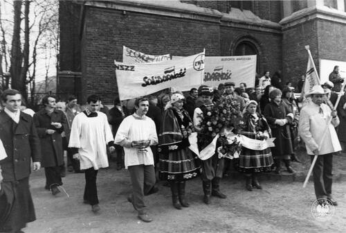 Na fotografii uczestnicy uroczystości - m innymi: mężczyzna i dwie kobiety w tradycyjnych strojach łowickich, księża, przedstawiciele hutników. Widoczne są też transparenty NSZZ Solidarność Budopol Warszawa oraz NSZZ Solidarność Zakładów Wytwórczych Aparatury Wysokiego Napięcia w Warszawie. (fot. AIPN)