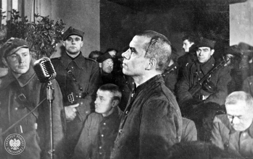 Proces członków załogi KL Lublin (Majdanek) przed polskim Specjalnym Sądem Karnym w Lublinie. Przed mikrofonem zeznający Edmund Pohlmann (z zakrwawioną głową). Ten były kapo KL Lublin uniknął kary, gdyż 29 XI 1944 r. popełnił samobójstwo. Lublin, między 27 a 29 XI 1944 r. (fot. z zasobu IPN)