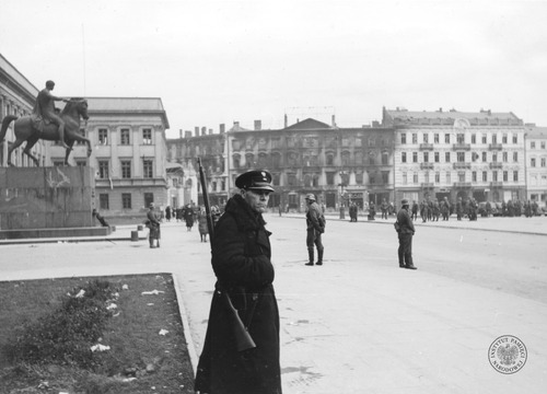 Policjant na posterunku przez pałacem Saskim - widok w kierunku północnym; 2 października 1939 roku. Po prawej pomnik księcia Józefa Poniatowskiego. W głębi grupy żołnierzy niemieckich na placu Piłsudskiego. W tle budynki przy ulicy Ossolińskich: spalone narożne kamienice u wylotu ulicy Wierzbowej (Wierzbowa 2 i Ossolińskich 8 - dawny budynek Petersburskich Towarzystw Ubezpieczeniowych), obok tzw. Dom Franckich przy ulicy Ossolińskich 6 i fragment kamienicy przy ulicy Ossolińskich 4. Autor: Kreutzer XX (samodzielny pluton propagandowy Luftwaffe. Prusy Wschodnie)
