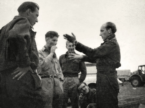 Dyskusja o taktyce walk powietrznych. Gestykuluje kpt. Stanisław Skalski, a przysłuchują się, od lewej: kpt. Karol Pniak, por. Eugeniusz Horbaczewski (zwany „Dziubkiem”), st. sierż. Władysław Majchrzyk i (przykucnięty) por. Ludwik Martel. W głębi zdjęcia widać sprzęt transportowy ich mobilnej jednostki lotniczej