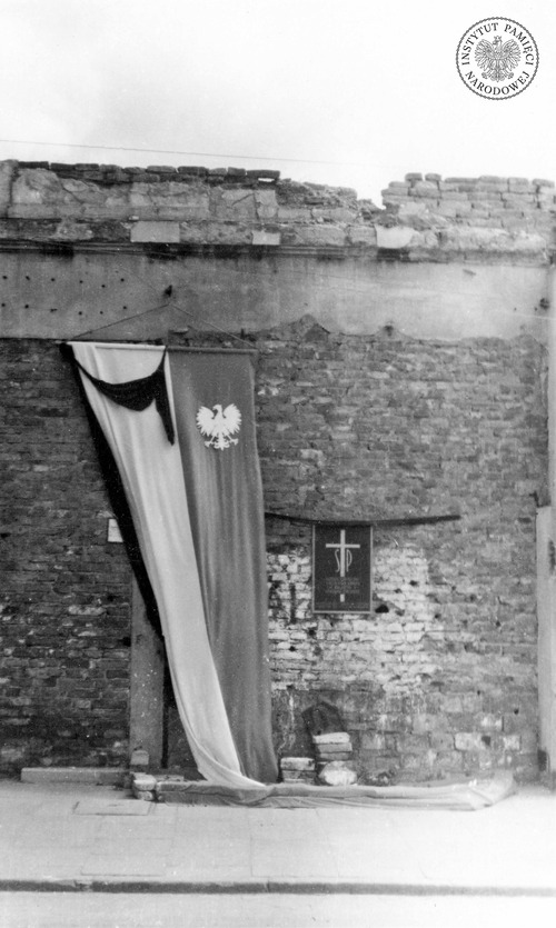 Miejsce egzekucji mieszkańców Warszawy upamiętnione czarną, blaszaną płytą pamiątkową z białym krzyżem umiejscowionym pomiędzy literami: Ś i P. Zdjęcie wykonano prawdopodobnie w lipcu 1945 r. przy ul. Nowy Świat w Warszawie (fot. z zasobu IPN)