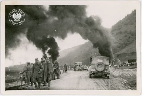 Żołnierze jugosłowiańscy wracają do domów po zakończeniu walk z Niemcami po agresji III Rzeszy na Jugosławię, kwiecień 1941 r. W tle pożar składu benzyny (fot. z zasobu AIPN)