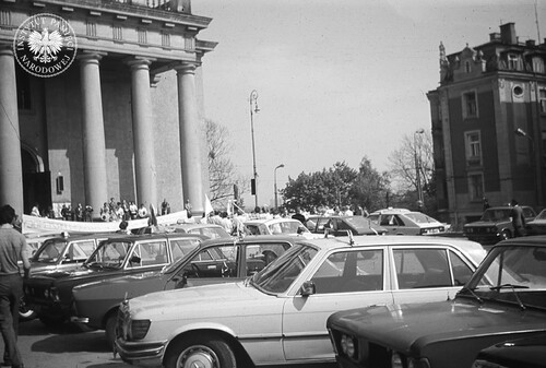 Uroczysty przejazd lubelskich taksówkarzy ulicami miasta w intencji zdrowia Jana Pawła II po zamachu na jego życie. Na zdjęciu kilkanaście taksówek przed lubelską archikatedrą św. Jana Chrzciciela i św. Jana Ewangelisty, po prawej widoczna jedna z kamienic przy ul. Królewskiej. Lublin, pl. Katedralny, maj 1981 r. (fot. z zasobu AIPN)