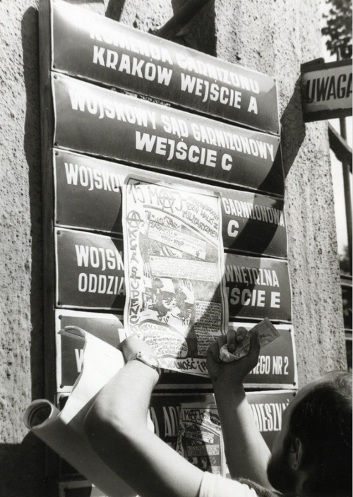 J. Rojek nakleja plakat AS WiP na bramie prowadzącej do kompleksu wojskowego  przy ul. Rakowickiej 22 w Krakowie, 15 V 1989 (fot. AIPN)