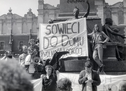 Wiec na Rynku Głównym w Krakowie w dniu 16 V 1989 r. pod hasłem „Sowieci do domu”. Od lewej stoją: J. Skoczylas (niezależny dziennikarz) J. Rojek, M. Gryczmańska (z tubą), Z. Przytuła (w środku, trzyma transparenty) R. Huget (przemawia), R. Młynarczyk (na stopniach pomnika, w długich włosach, trzyma transparent) (fot. AIPN)