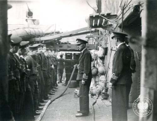 Kmdr por. Dzienisiewicz przemawia do załogi przed operacją lądowania w Normandii, czerwiec 1944 r. W operacji Neptune – fazie desantu z morza – wzięło udział ponad 1200 okrętów, 4100 jednostek desantowych, 1600 okrętów pomocniczych i statków handlowych. Wśród nich – oprócz Dragona – znalazły się cztery polskie niszczyciele: Błyskawica, Piorun, Ślązak i Krakowiak oraz polskie statki transportowe. Kopia cyfrowa fotografii pozyskana ze zbiorów Stowarzyszenia Weteranów Armii Polskiej w Ameryce (fot. z zasobu IPN)