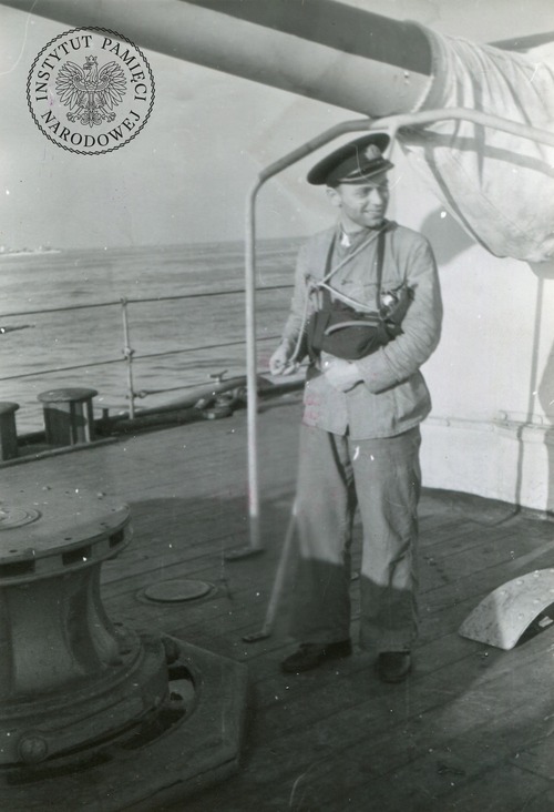 Ppor. mar. Zdzisław Szwede, IV oficer mechanik ORP Dragon, na tle rufowej wieży artylerii, 1944 r. Na pokładzie okrętu służyło 21 oficerów. W ataku niemieckiej „żywej torpedy” poległ jeden z nich, ponadetatowy oficer wachtowy Karol Marks, pośmiertnie mianowany porucznikiem. Kopia cyfrowa ze zbiorów Stowarzyszenia Weteranów Armii Polskiej w Ameryce (z zasobu IPN)