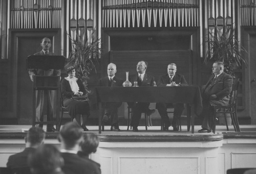 The Presidium of the Congress of Polish Choir Singers from Poland and Abroad in Warsaw. Apoloniusz Zarychta, Head of the Emigration Policy Department of the Ministry of Foreign Affairs, is speaking in the Warsaw Conservatory hall. Seated from left: Franciszek Ratke (USA); Antoni Ponikowski (former Polish Prime Minister), Professor at the Warsaw University of Technology; Leon Surzyński, President of the Greater Poland Association of Singing Clubs; Bronisław Hełczyński, Deputy President of the World Association of Poles Abroad; Przybyłski. Warsaw, 1936. (Photo from the National Digital Archives)