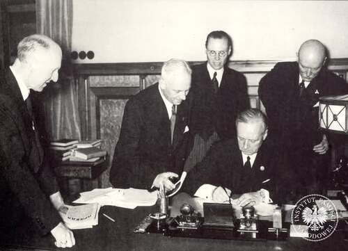 Minister spraw zagranicznych III Rzeszy Joachim von Ribbentrop (siedzi) podpisuje niemiecko-sowiecki pakt o nieagresji (tzw. pakt Ribbentrop-Mołotow). Wśród otaczających go osób stoi ambasador III Rzeszy w Moskwie Friedrich-Werner von der Schulenburg (pierwszy od prawej, pochylony). Zdjęcie ze zbioru kopii cyfrowych fotografii dokumentujących wydarzenia II wojny światowej, pozyskanego z Narodowej Agencji Archiwów i Nagrań w College Park w stanie Maryland w USA (fot. z zasobu AIPN)