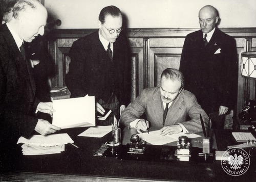 Ludowy komisarz spraw zagranicznych ZSRS Wiaczesław Mołotow (pośrodku, siedzi) składa podpis na dokumencie niemiecko-sowieckiego paktu o nieagresji (tzw. paktu Ribbentrop-Mołotow). Wokół stoi trzech mężczyzn w garniturach, w tym (po prawej) ambasador III Rzeszy w Moskwie Friedrich-Werner von der Schulenburg. Zdjęcie ze zbioru kopii cyfrowych fotografii dokumentujących wydarzenia II wojny światowej, pozyskanego z Narodowej Agencji Archiwów i Nagrań w College Park w stanie Maryland w USA (fot. z z