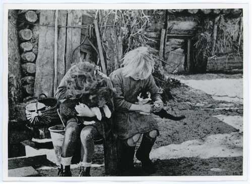 Dwie dziewczynki, trzymające na rękach kota i psa, siedzą przed chatą w podwarszawskim Rembertowie w 1945 r. (fot. z zasobu AIPN)