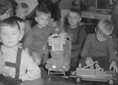 Gromada przedszkolaków siedzi na podłodze. Dwóch chłopców (z prawej) bawi się autkiem oraz kolejką z doczepioną fotografią Józefa Stalina z napisem: „OFENSYWA POKOJU” (fot. z zasobu IPN)