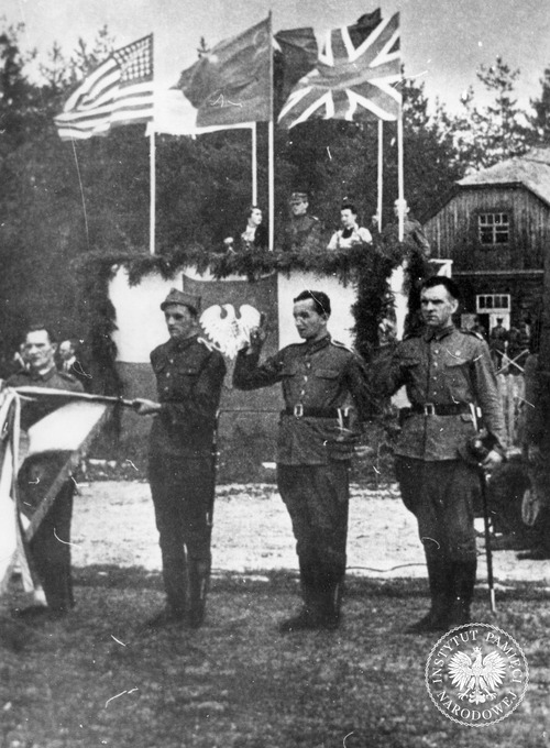 Przysięga 1. Dywizji Piechoty w Sielcach nad Oką (ZSRS). Na zdjęciu: poczet sztandarowy, w głębi na trybunie honorowej, od lewej – przewodnicząca ZPP Wanda Wasilewska, dowódca dywizji gen. Zygmunt Berling, kapelan ks. Wilhelm Kubsz oraz N.N. żołnierz (salutuje), nad nimi flagi USA, ZSRS i Wielkiej Brytanii. 15 lipca 1943 r. Fot. z zasobu IPN