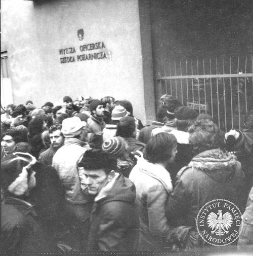 Strajk podchorążych w Wyższej Oficerskiej Szkole Pożarniczej na warszawskim Żoliborzu, przy ul. Słowackiego. Na zdjęciu grupa osób przed bramą uczelni blokowaną przez oddział Zmotoryzowanych Odwodów Milicji Obywatelskiej. Warszawa, 2 grudnia 1981 r. (fot. z zasobu AIPN)