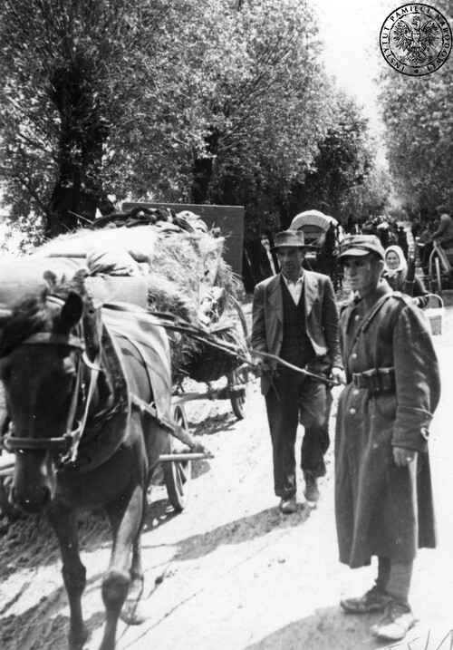 Kolumna przesiedleńców ukraińskich na drodze do jednego z punktów zbornych (kwiecień-czerwiec 1947 r.). Po prawej żołnierz komunistycznej armii pilnuje porządku. Fot. z zasobu IPN