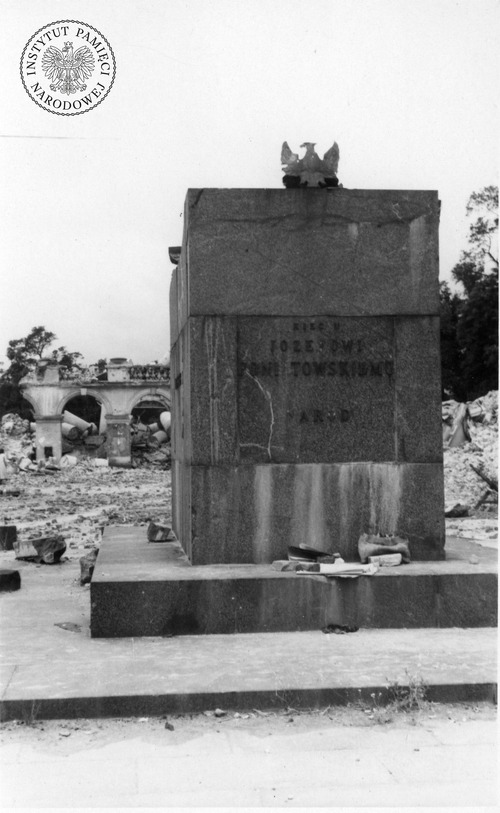 Cokół obalonego pomnika księcia Józefa Poniatowskiego w czerwcu 1945 r. W tle ruiny zburzonego Pałacu Saskiego i Grobu Nieznanego Żołnierza. Napis pozbawiony niektórych liter Xięcu | Józe[f]owi | Poni[a]towskiemu | [N]ar[ó]d (fot. z zasobu IPN)