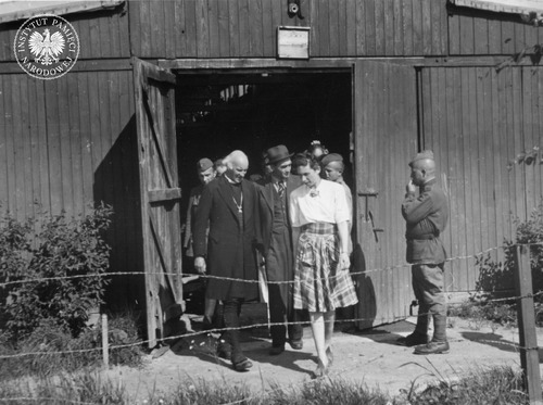 Delegacja angielska z dr H. Johnsonem (pierwszy od lewej) zwiedza jeden z baraków byłego KL Auschwitz-Birkenau. Delegację po baraku oprowadza sędzia Komisji Oświęcimskiej Jan Sehn (w środku, w kapeluszu), 29 maja 1945 r. (fot. z zasobu AIPN)