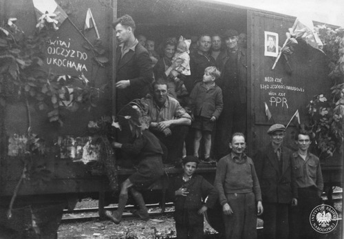 Zdjęcie z albumu Państwowego Urzędu Repatriacyjnego, Oddziału Katowice, dotyczące powojennej „repatriacji” Polaków. Przybysze z dawnych Kresów Wschodnich, pozbawieni rodzinnych domów, byli przedstawiani jako szczęśliwi z przybycia do ojczyzny pod rządami Polskiej Partii Robotniczej. Miały tego dowodzić dekoracje i napisy na wagonie. Górny Śląsk, 1945–1946 (z zasobu AIPN)
