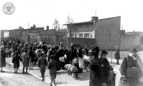 Grupa mieszkańców łódzkiego getta prawdopodobnie w drodze na stację kolejową Radogoszcz (niem. Radegast), skąd odjeżdżały transporty do obozów koncentracyjnych i obozów zagłady. Dorośli dźwigają bagaże z dobytkiem, ponieważ wmawiano im, że mają zostać „przesiedleni”. Maj 1942 r. (fot. z zasobu AIPN)
